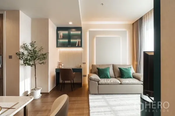 Condominium for rent in Khlong Toei, Bangkok - Cozy living room featuring a sofa and a built-in teal study desk with lit display cabinets.