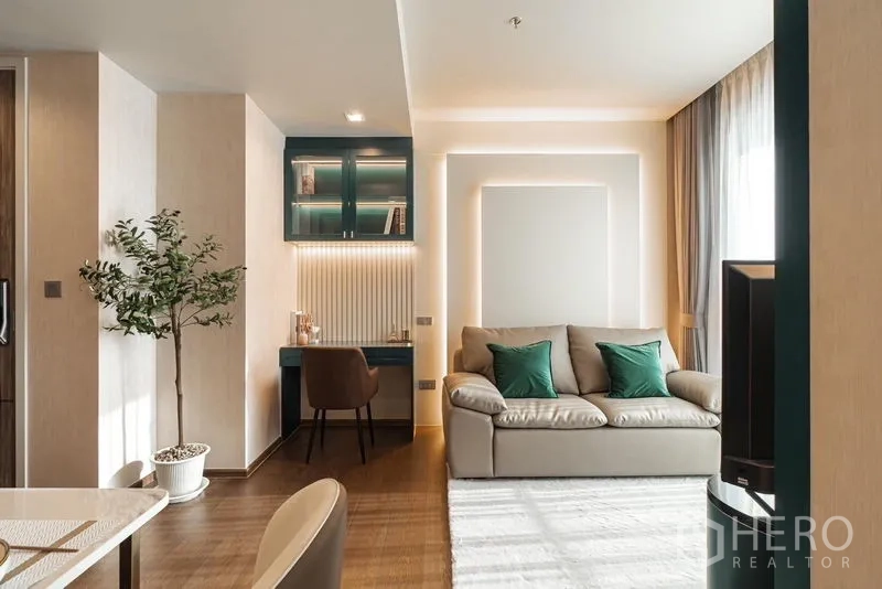 Condominium for rent in Khlong Toei, Bangkok - Cozy living room featuring a sofa and a built-in teal study desk with lit display cabinets.