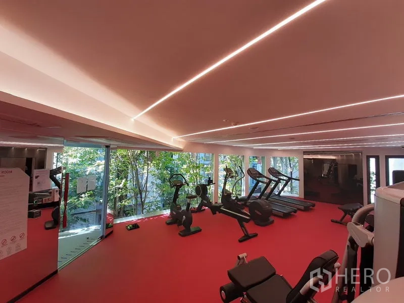 公寓 出租或出售在Watthana, Bangkok - 明亮健身房，跑步机与动感单车，透过大窗可见花园景。