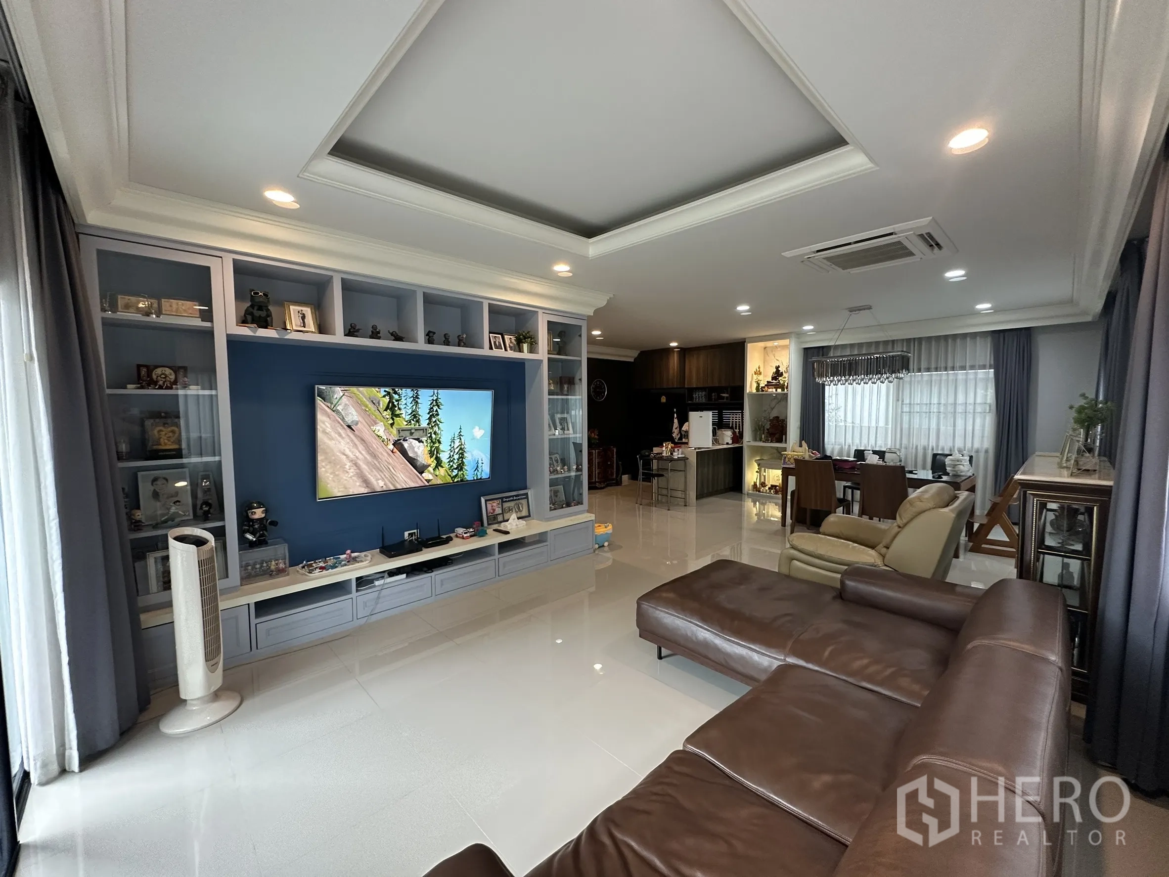 Detached House for rent in Lam Luk Ka, Pathum Thani - Open-plan living room with built-in TV wall and brown leather sectional.