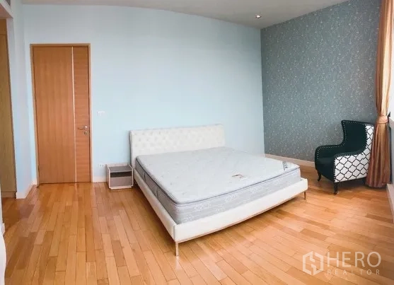 Condominium for rent or sale in Khlong Toei, Bangkok - Spacious bedroom with wood floors, upholstered bed frame and patterned feature wall.