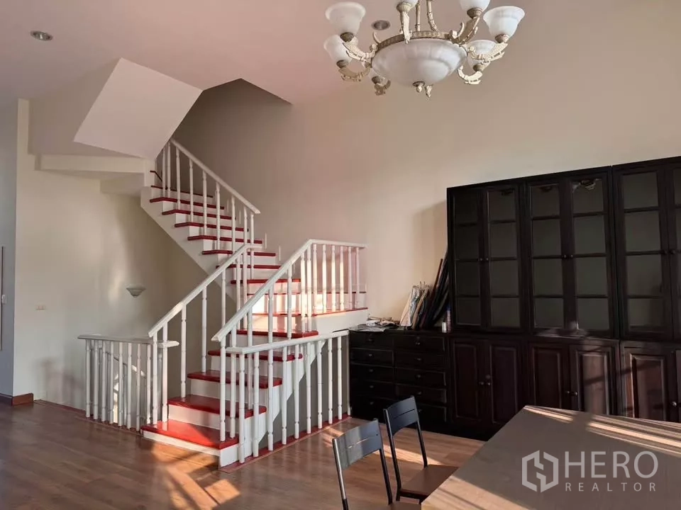 Townhouse for rent in Bang Kho Laem, Bangkok - Double-height living area featuring a white staircase, chandelier and dark built-in cabinets.