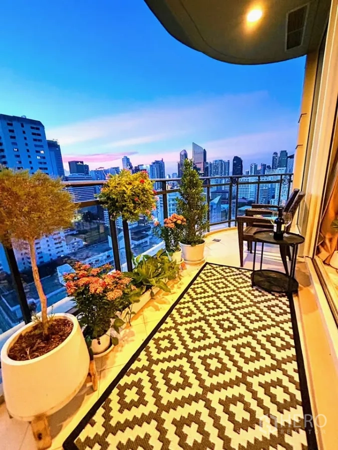 Condominium for sale in Watthana, Bangkok - Balcony garden at dusk with potted plants, patterned rug and seating above the city.