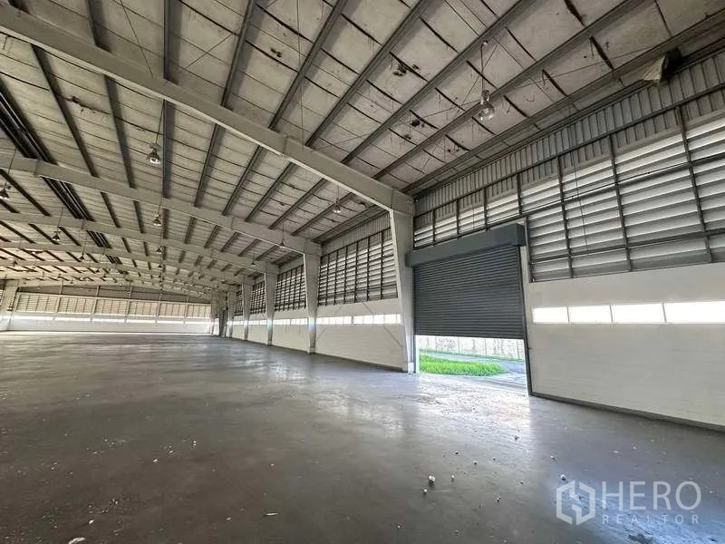 Factory for rent in Khlong Luang, Pathum Thani - Interior showing roller shutter loading door, ventilated walls and green verge outside.
