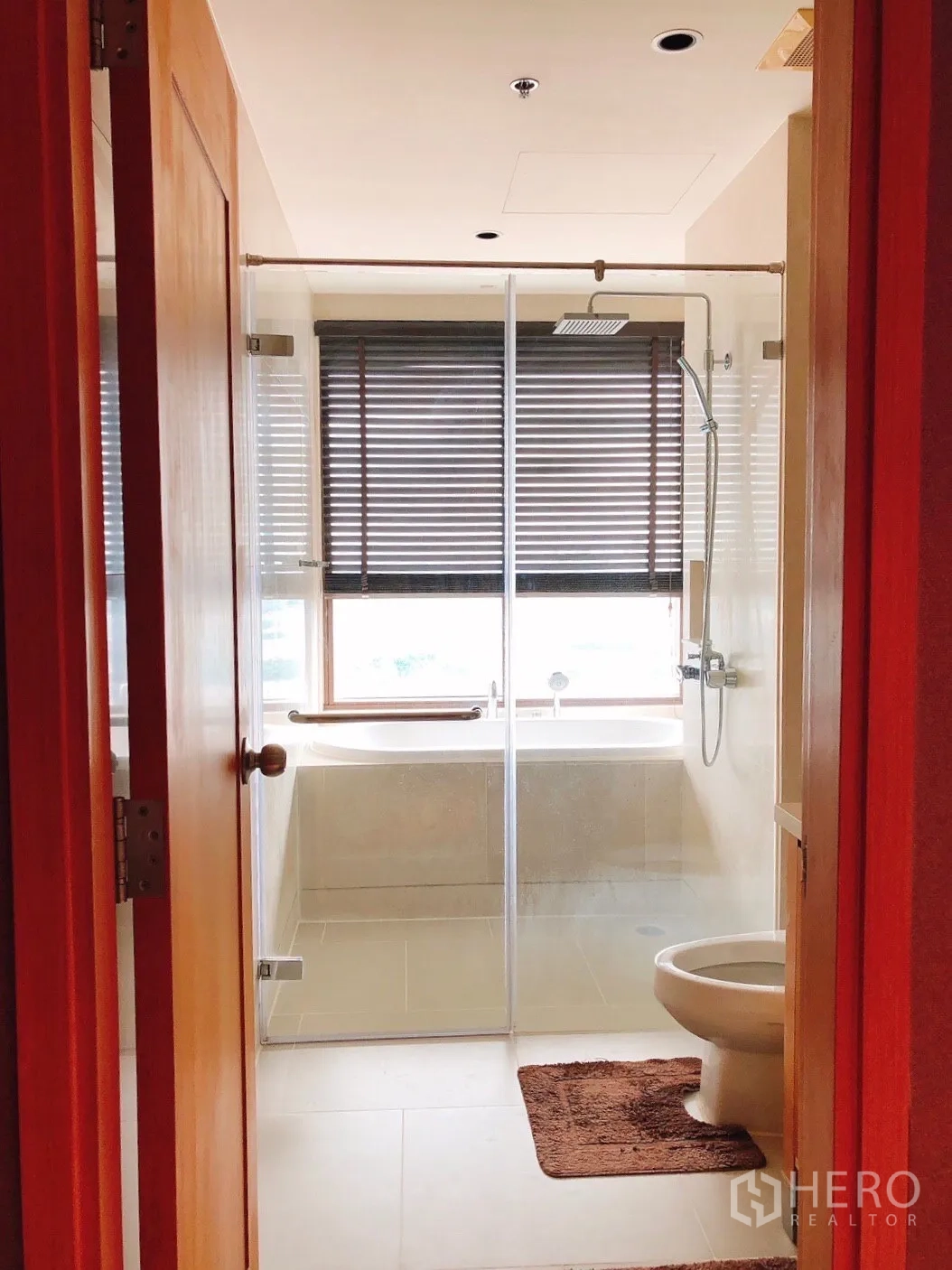 Condominium for rent in Khlong Toei, Bangkok - Bathroom with glass shower enclosure and bathtub by the window.