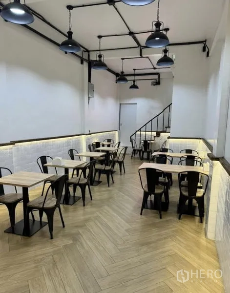 Shophouse for rent in Khlong Toei, Bangkok - Dining area with tables and metal chairs beneath industrial pendant lights.