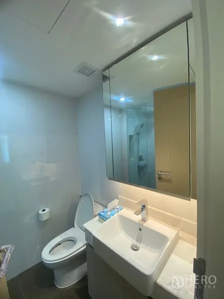 Apartment for rent in Watthana, Bangkok - Secondary bathroom with single vanity, mirror cabinet and toilet in a clean modern style.