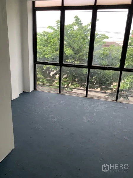 Shophouse for rent in Bang Na, Bangkok - Room with floor-to-ceiling windows overlooking trees and the street.