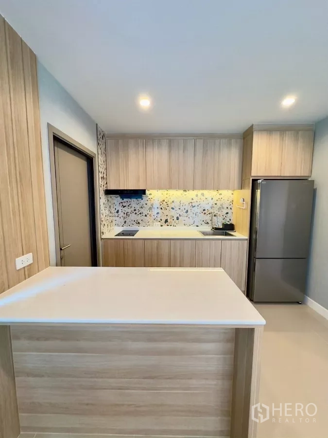 Detached House for rent in Samut Prakan - Light-wood kitchen with island, terrazzo backsplash and refrigerator.