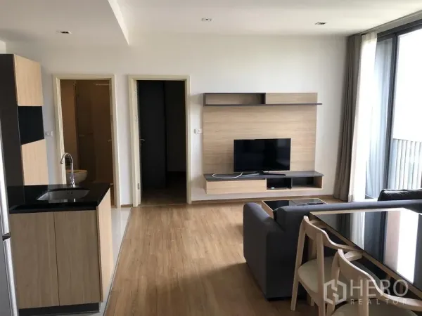 Condominium for rent in Watthana, Bangkok - Bright living room with TV console, floor‑to‑ceiling window, and doors leading to bedrooms and a bathroom.