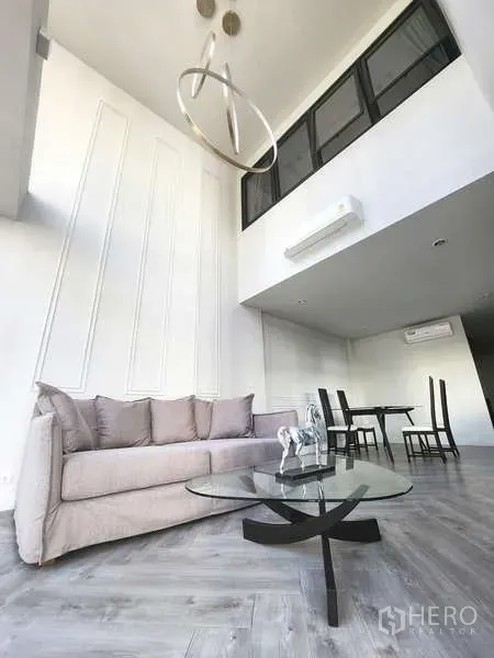 ทาวน์เฮาส์ ให้เช่าในWatthana, Bangkok - ห้องรับแขกเพดานสูง โซฟาสีเทา โต๊ะกระจก โคมไฟโมเดิร์น และพื้นที่ทานอาหารต่อเนื่อง