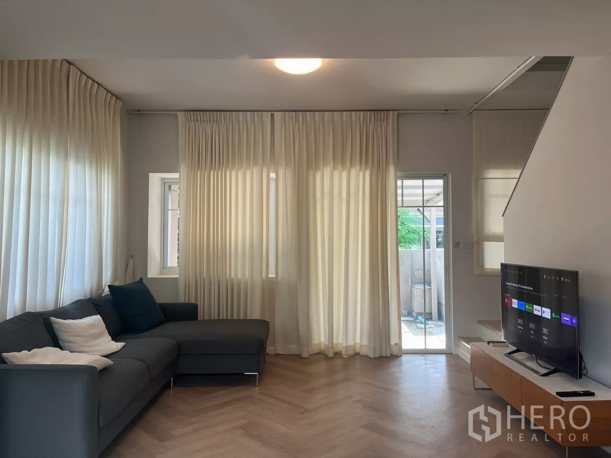 Townhouse for rent in Bang Phli, Samut Prakan - Bright living room with sheer curtains, sliding door, sectional sofa and TV.