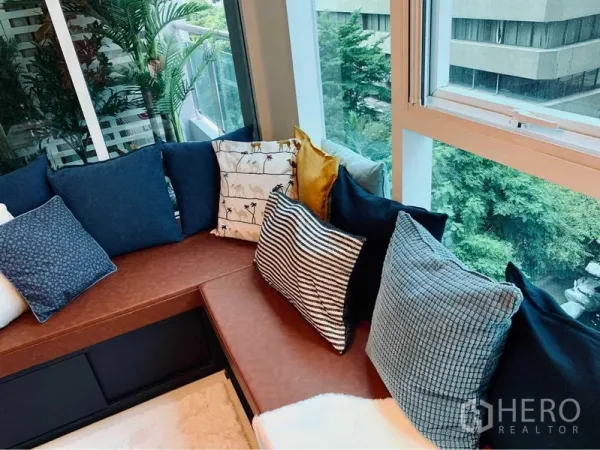 公寓 出租在Watthana, Bangkok - 转角飘窗长凳摆放多款靠垫，窗外可见葱郁树景。