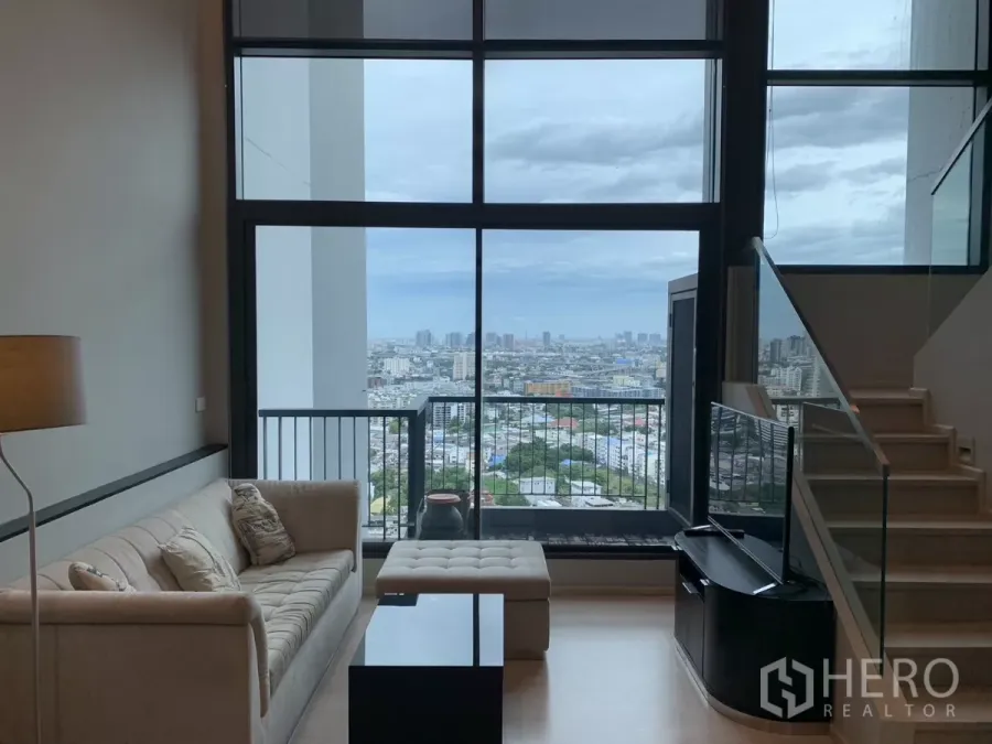 公寓 出租在Khlong Toei, Bangkok - 沙发与电视面向整面落地窗，阳台眺望城市天际线的阁楼式客厅。