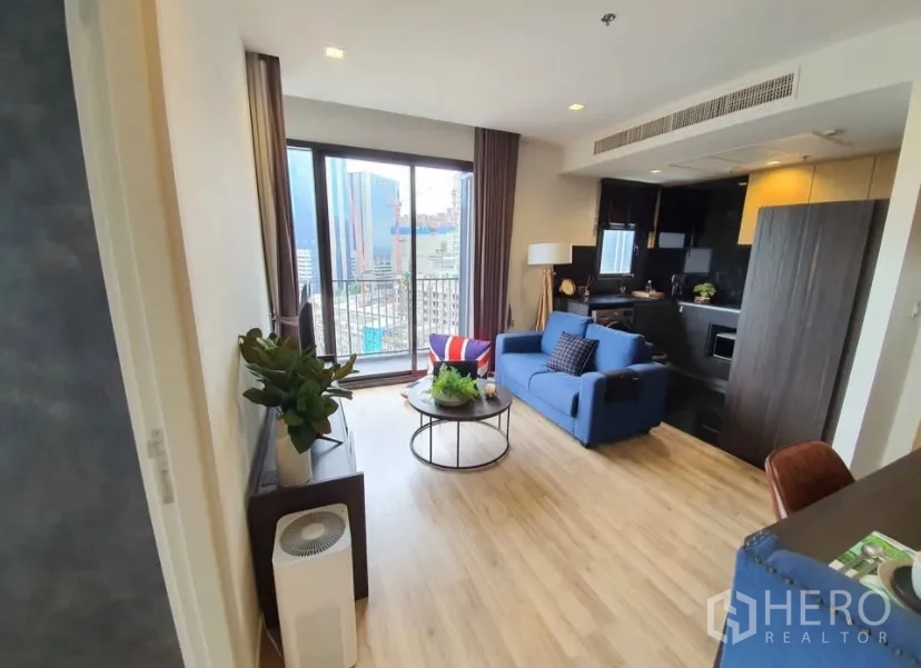 คอนโด for rent in Chatuchak, Bangkok - พื้นที่นั่งเล่นมีโซฟาสีน้ำเงิน โต๊ะกลางทรงกลม และประตูกระจกสไลด์ออกไประเบียง