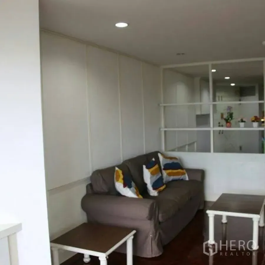 公寓 出租在Watthana, Bangkok - 明亮客厅，灰色沙发与彩色抱枕，嵌入式隔断与木地板，邻近厨房。