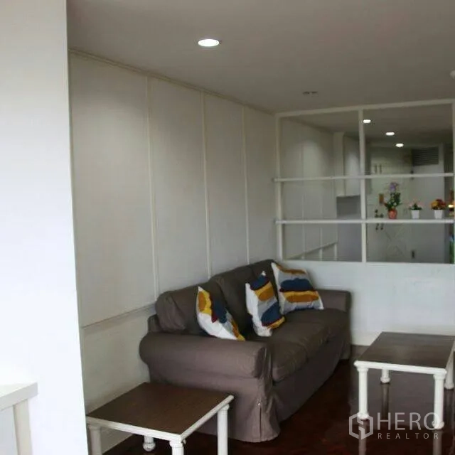 公寓 出租在Watthana, Bangkok - 明亮客厅，灰色沙发与彩色抱枕，嵌入式隔断与木地板，邻近厨房。