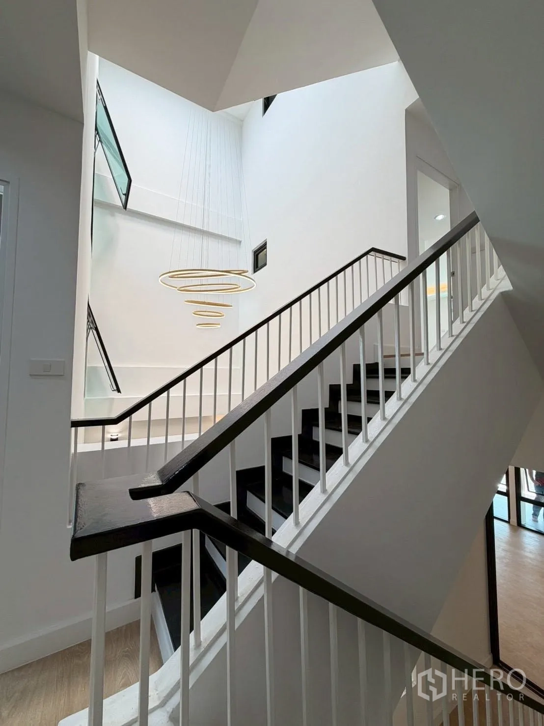 Townhouse for sale in Phra Khanong, Bangkok - Staircase rising around a tall atrium with a modern ring chandelier.