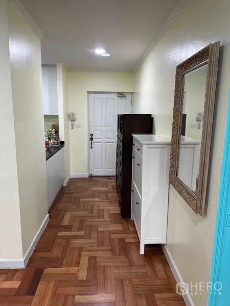 Condominium for sale in Bangkok - Entry corridor with wood parquet flooring, wall mirror and cabinets leading to kitchen.