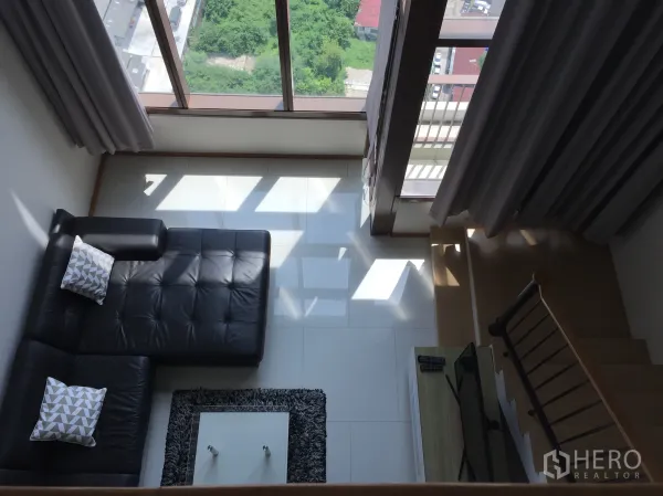 Condominium for rent in Khlong Toei, Bangkok - Double-height living room with floor-to-ceiling windows, L-shaped leather sofa and stairs.