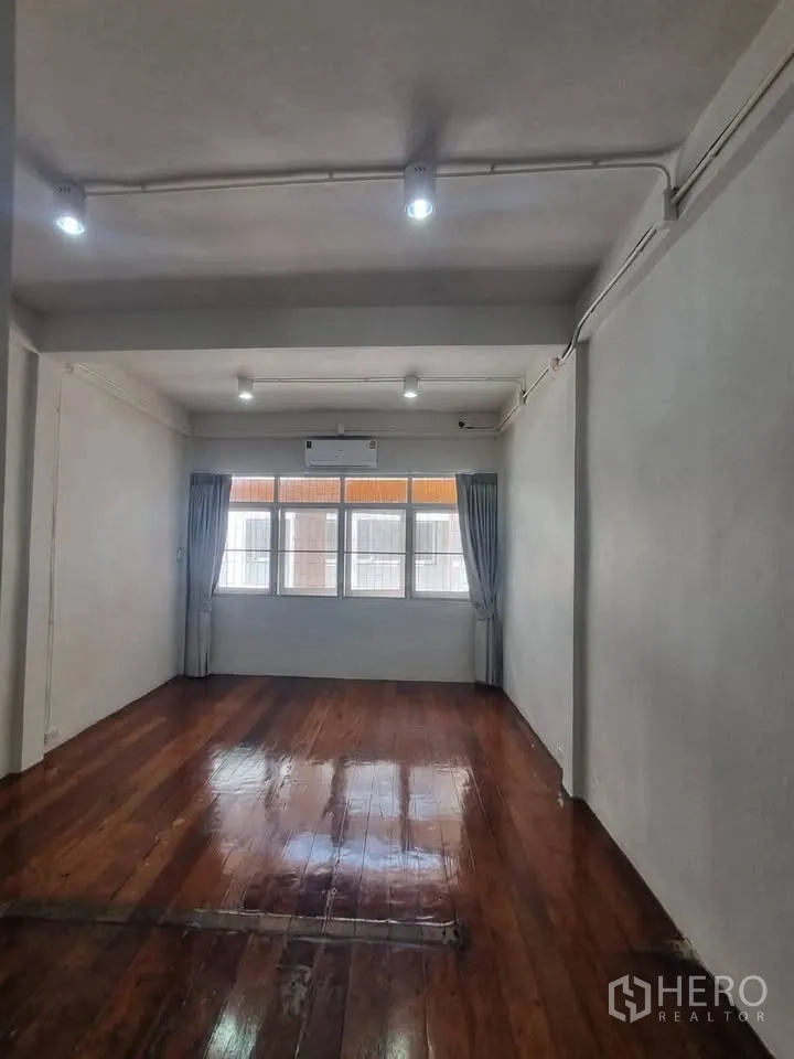 Shophouse for rent in Phra Khanong, Bangkok - Bright room with wooden flooring, large curtained windows, and ceiling spotlights.