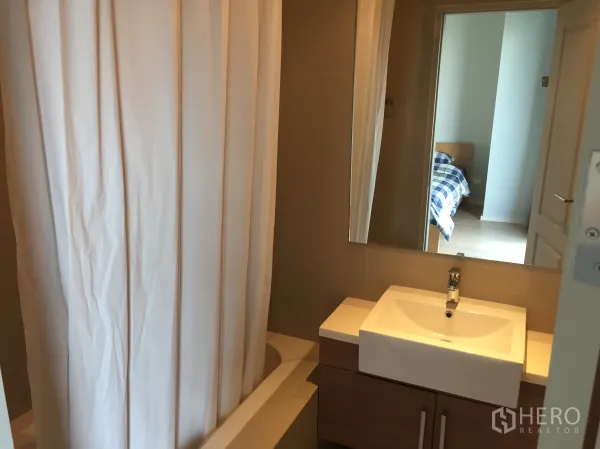 Condominium for rent in Bangkok - Modern bathroom with sink, large mirror and shower-over-bathtub with curtain.