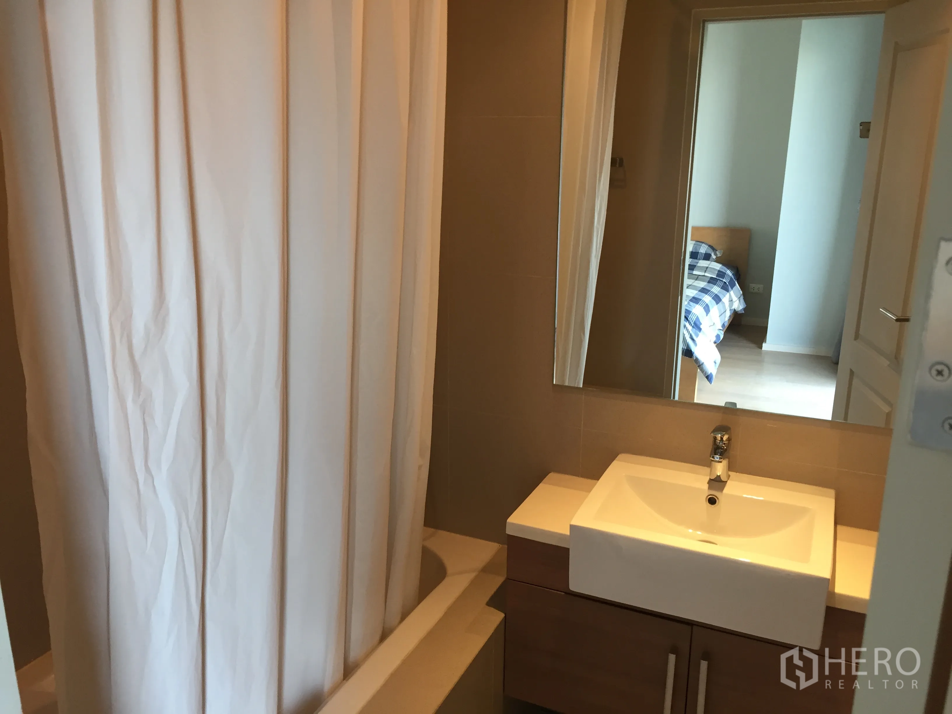 Condominium for rent in Bangkok - Modern bathroom with sink, large mirror and shower-over-bathtub with curtain.