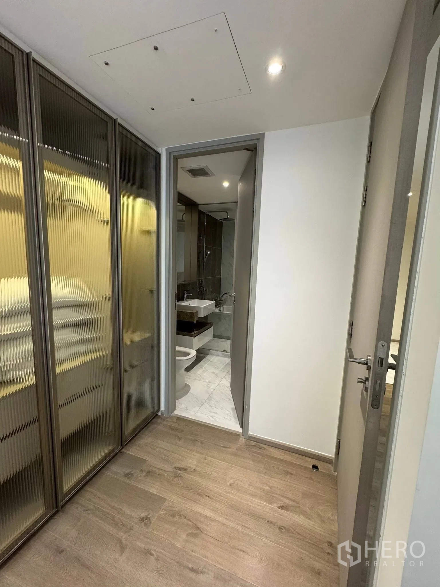 公寓 for rent in Khlong Toei, Bangkok - 入口走廊设条纹玻璃衣柜，通往铺大理石地砖的浴室。
