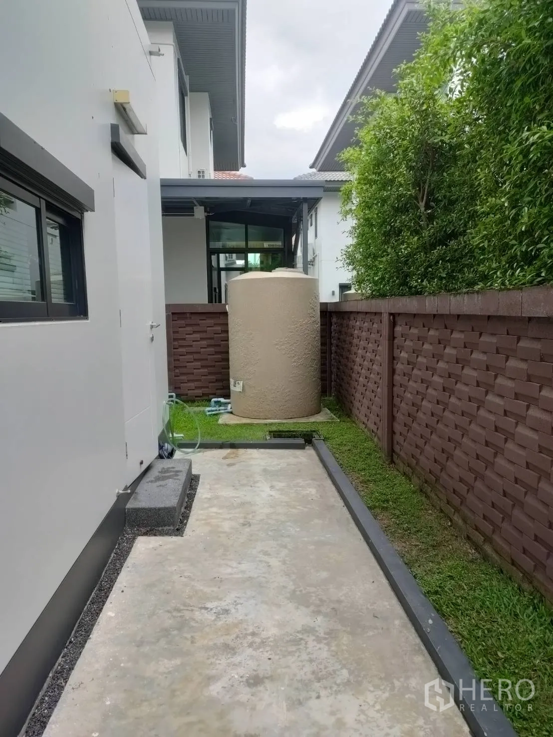 Detached House for rent or sale in Lam Luk Ka, Pathum Thani - Service side yard with concrete pad, water tank, and high privacy wall.