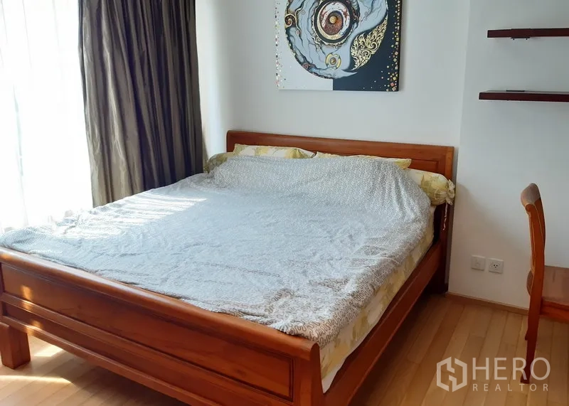 Condominium for rent in Khlong Toei, Bangkok - Cozy bedroom with large wooden bed, wall art and floor-to-ceiling curtains.