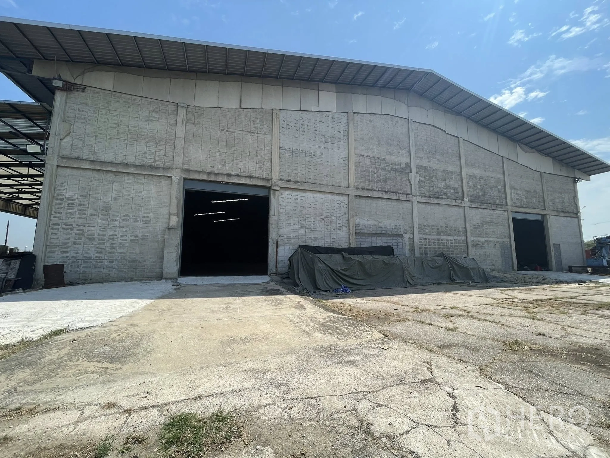 Factory for rent in Bang Bua Thong, Nonthaburi - Concrete factory exterior with metal roof, wide loading ramp, and open roller door.