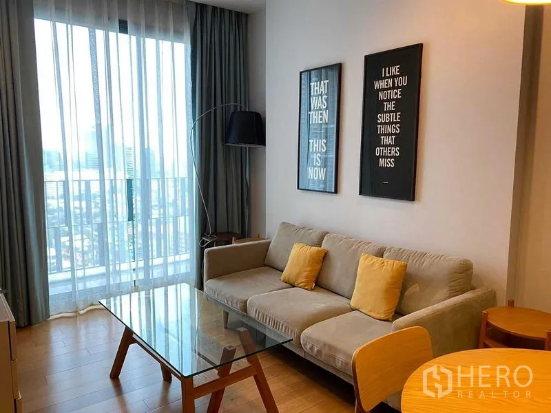 公寓 出租在Khlong Toei, Bangkok - 客厅设灰色沙发、玻璃茶几，落地窗外为城市景观。