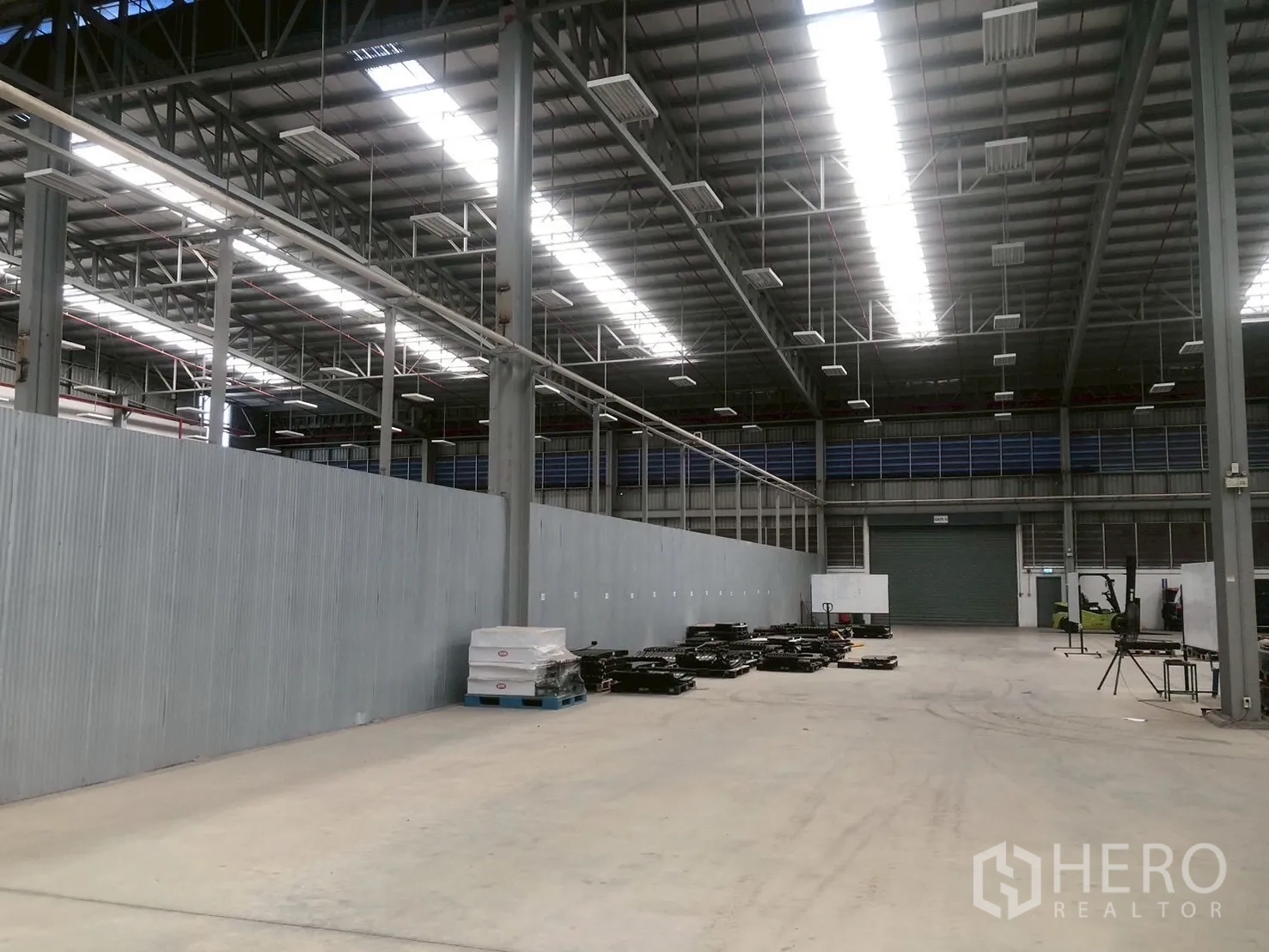 Factory for rent in Pluak Daeng, Rayong - Aisle inside the warehouse leading to a roller shutter door and partition wall under high-bay lights.