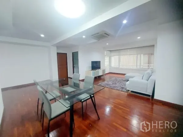 公寓 出租在Watthana, Bangkok - 开放式客餐厅，玻璃餐桌、白色沙发、电视柜与实木地板。
