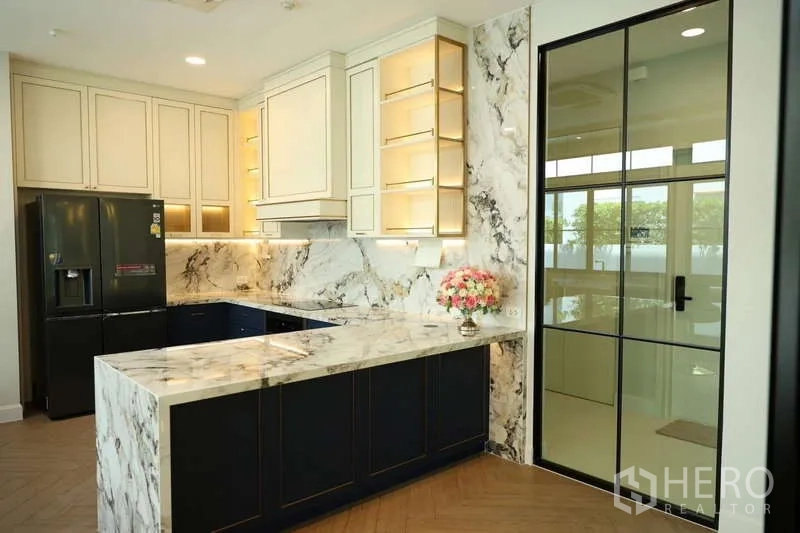 Detached House for rent or sale in Saphan Sung, Bangkok - Modern marble kitchen with L-shaped counter, black fridge and glass door.