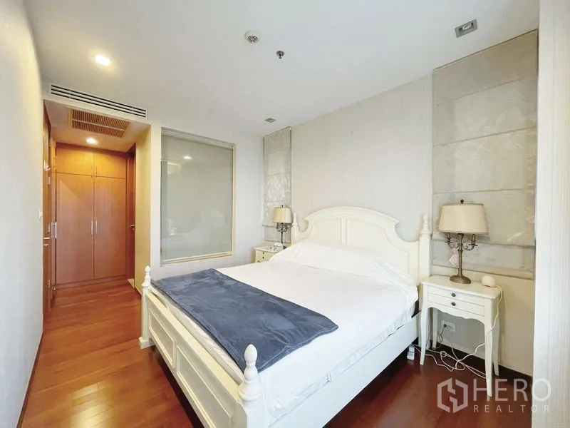 Condominium for sale in Khlong Toei, Bangkok - Cozy bedroom with white wooden bed, matching nightstands and corridor to built-in closet.