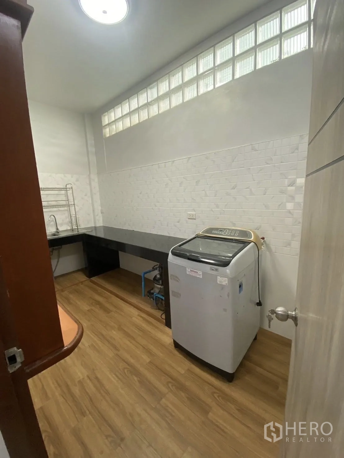 Townhouse for rent in Huai Khwang, Bangkok - Kitchen with wood-look flooring, long counter, glass-block clerestory windows, and washing machine.