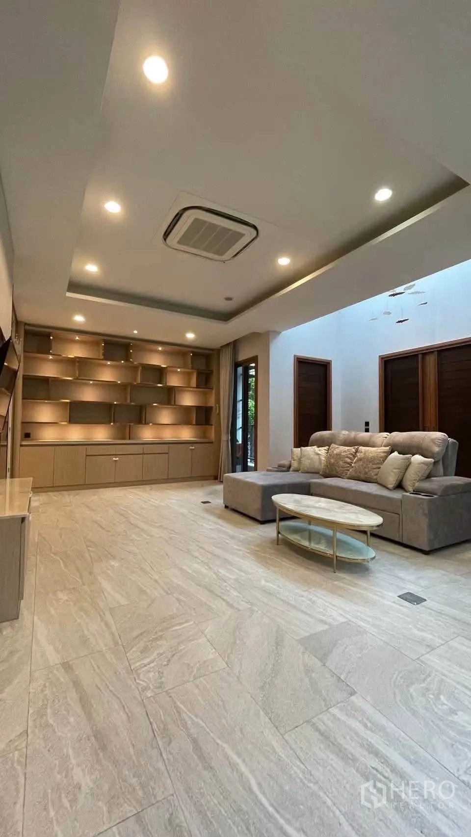 Detached House for rent in Prawet, Bangkok - Living area with built-in shelving wall, sectional sofa and recessed lighting.