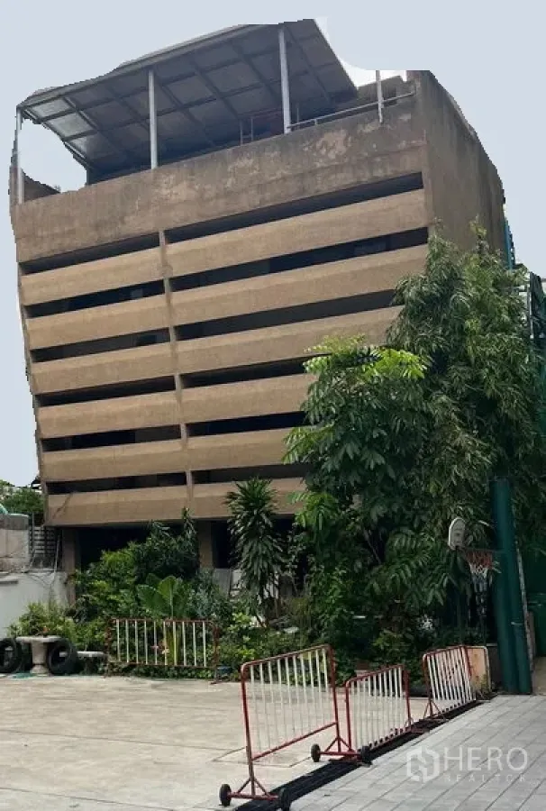 零售空间 出租在Khlong Toei, Bangkok - 多层混凝土建筑，水平百叶式立面，屋顶遮棚，一层前院有绿植与围栏，位于曼谷空堤区。