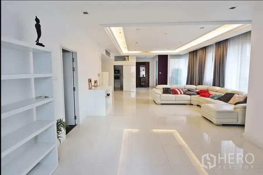 公寓 出租在Watthana, Bangkok - 宽敞的开放式客厅，白色转角沙发、吊顶灯、亮面地砖与大窗帘窗户。