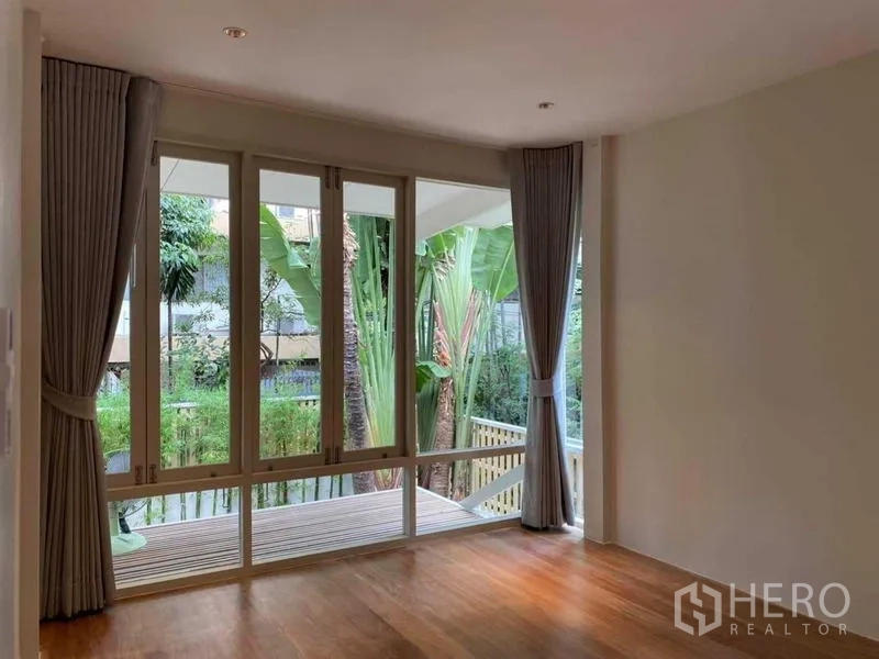 Detached House for rent in Watthana, Bangkok - Bright room with floor-to-ceiling windows overlooking a tropical garden.