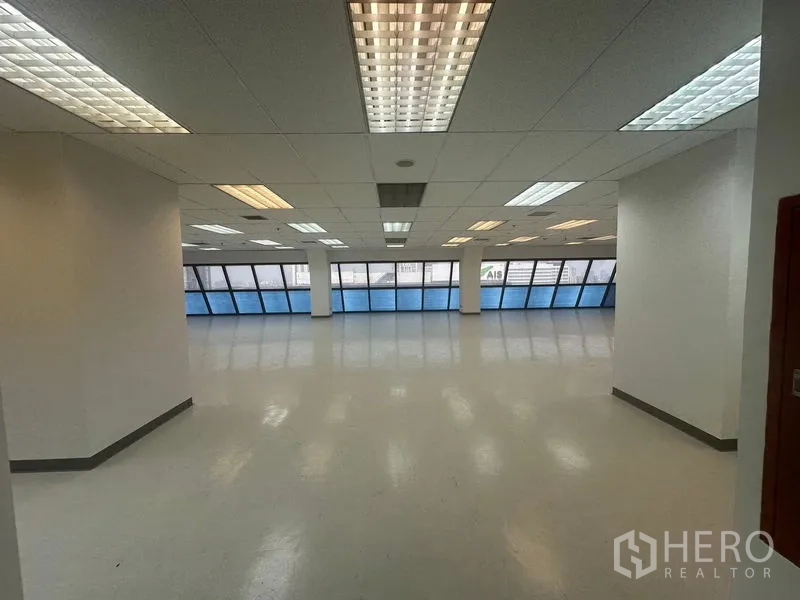 办公空间 出租在Phaya Thai, Bangkok - 开放式办公室，一侧为蓝色斜面带状窗，吊顶荧光灯照明充足。