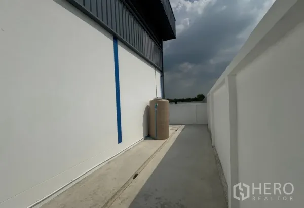 Warehouse for rent in Khlong Luang, Pathum Thani - Side service walkway with water storage tank and boundary wall.