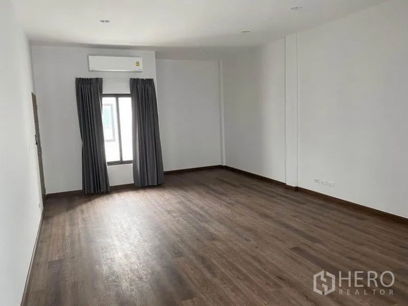Townhouse for rent in Bang Na, Bangkok - Large multipurpose room with wood floors, AC unit and a curtained window.