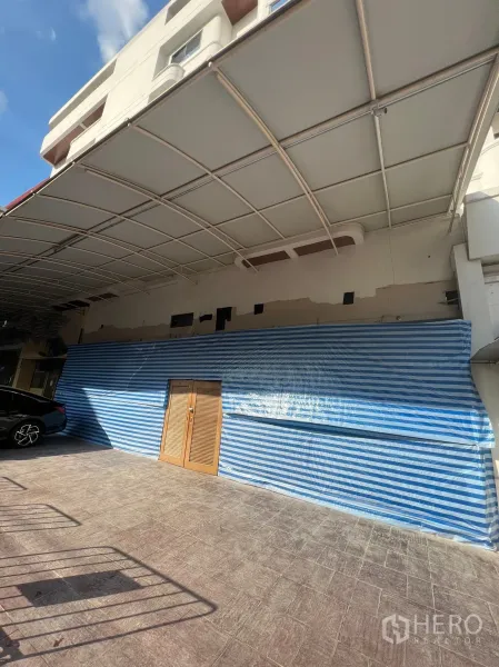 Retail Space for rent in Watthana, Bangkok - Ground-floor retail frontage at M Towers in Watthana with a wide canopy, blue striped temporary covering, wooden double doors, and forecourt parking.