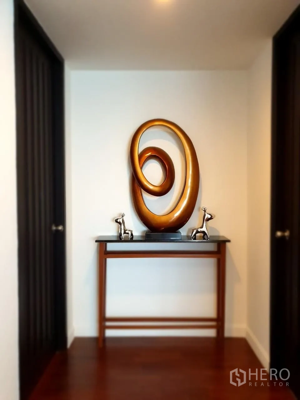 Apartment for rent in Bang Rak, Bangkok - Entry corridor with statement sculpture on console table and timber floors.