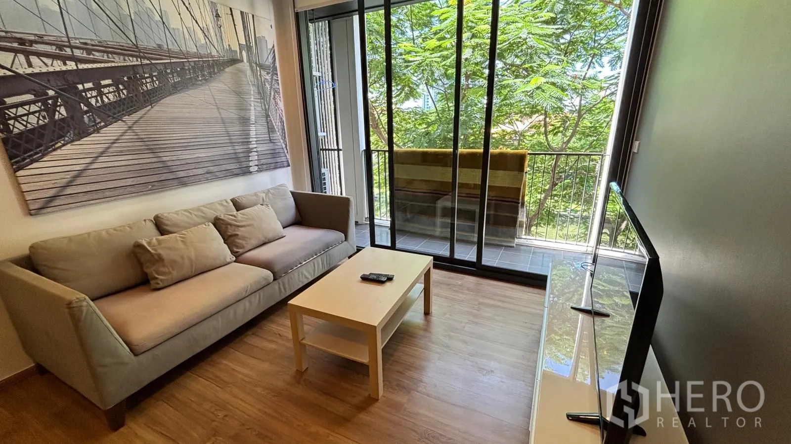 คอนโด for rent or sale in Watthana, Bangkok - ห้องนั่งเล่นสว่างมีภาพติดผนัง โต๊ะกลาง และหน้าต่างสูงจรดเพดานมองเห็นวิวเขียว