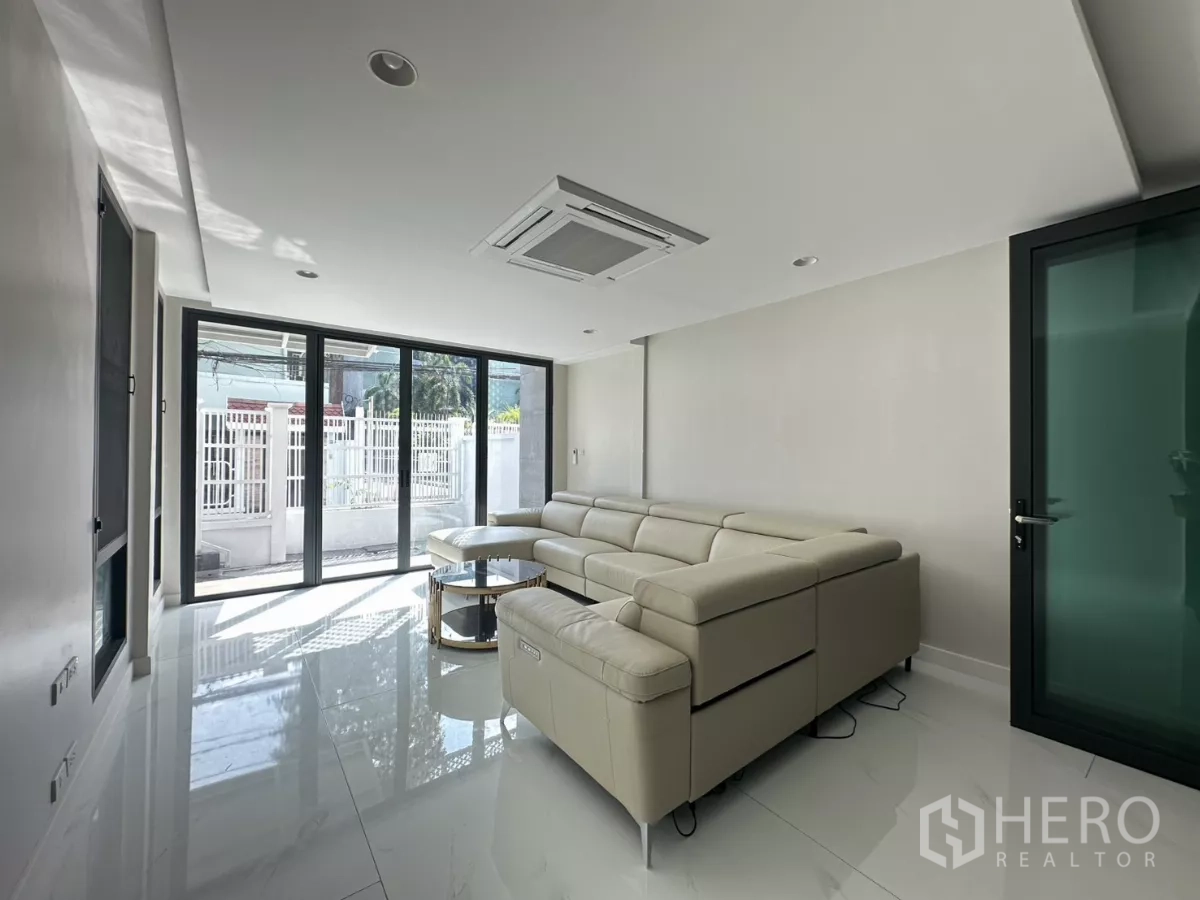 Townhouse for rent in Watthana, Bangkok - Sunlit lounge with sliding glass doors opening to the front terrace and gated fence.
