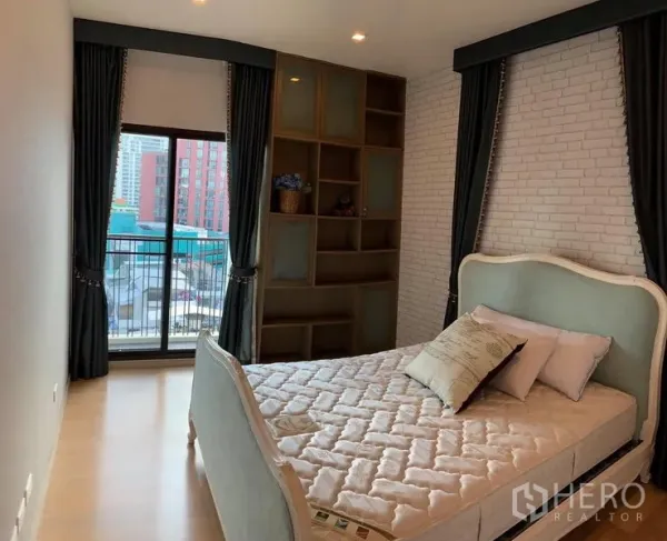 Condominium for rent in Phaya Thai, Bangkok - Cozy bedroom with upholstered bed, built-in shelving, and balcony access overlooking the city.