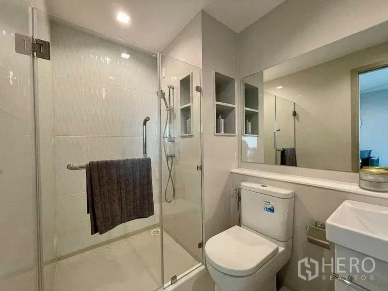 Condominium for rent in Chatuchak, Bangkok - Modern bathroom with glass-enclosed shower, vanity and built-in storage niches.